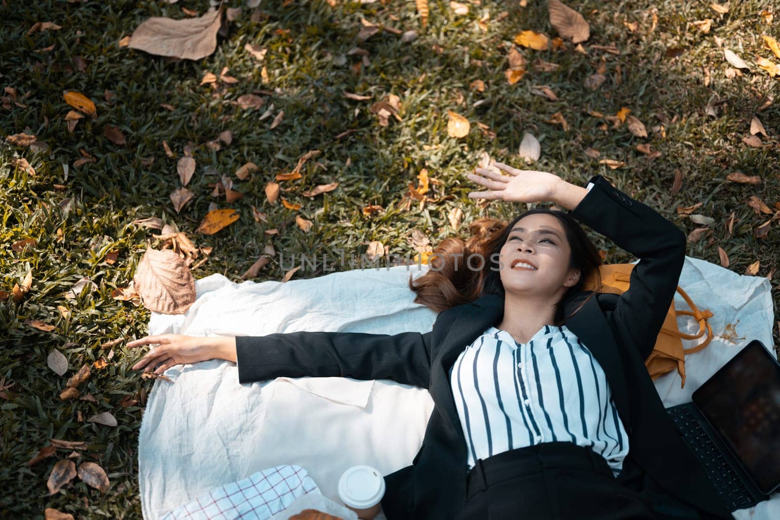 Happy beautiful businesswoman lying on grass chilling at garden or park in autumn. Overhead view.