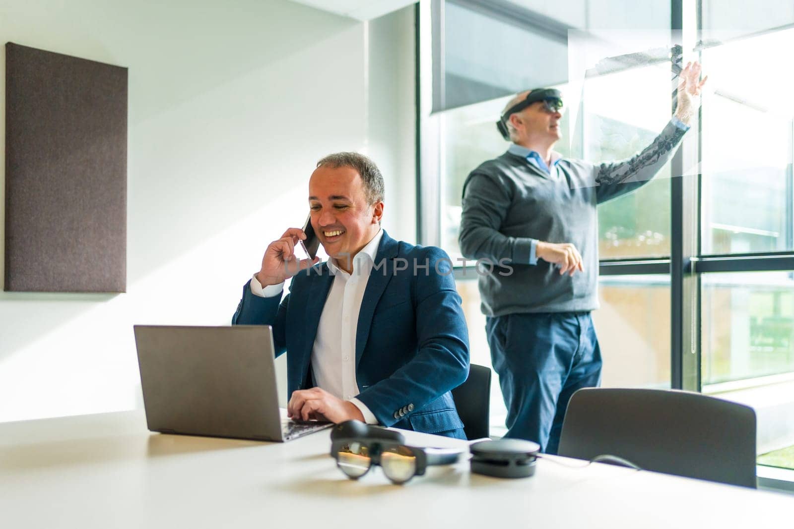 Businessmen using virtual touchscreen and laptop in the office while wearing mixed augmented vision goggles