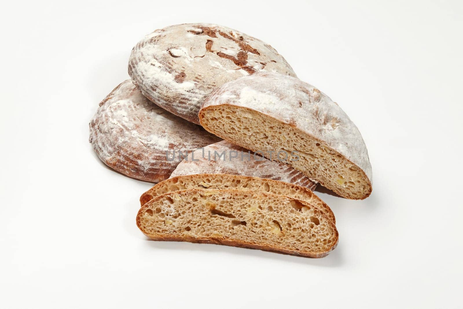 Close-up of whole and sliced freshly baked artisan sourdough round bread with crispy crust dusted with flour and airy soft texture, isolated on white background