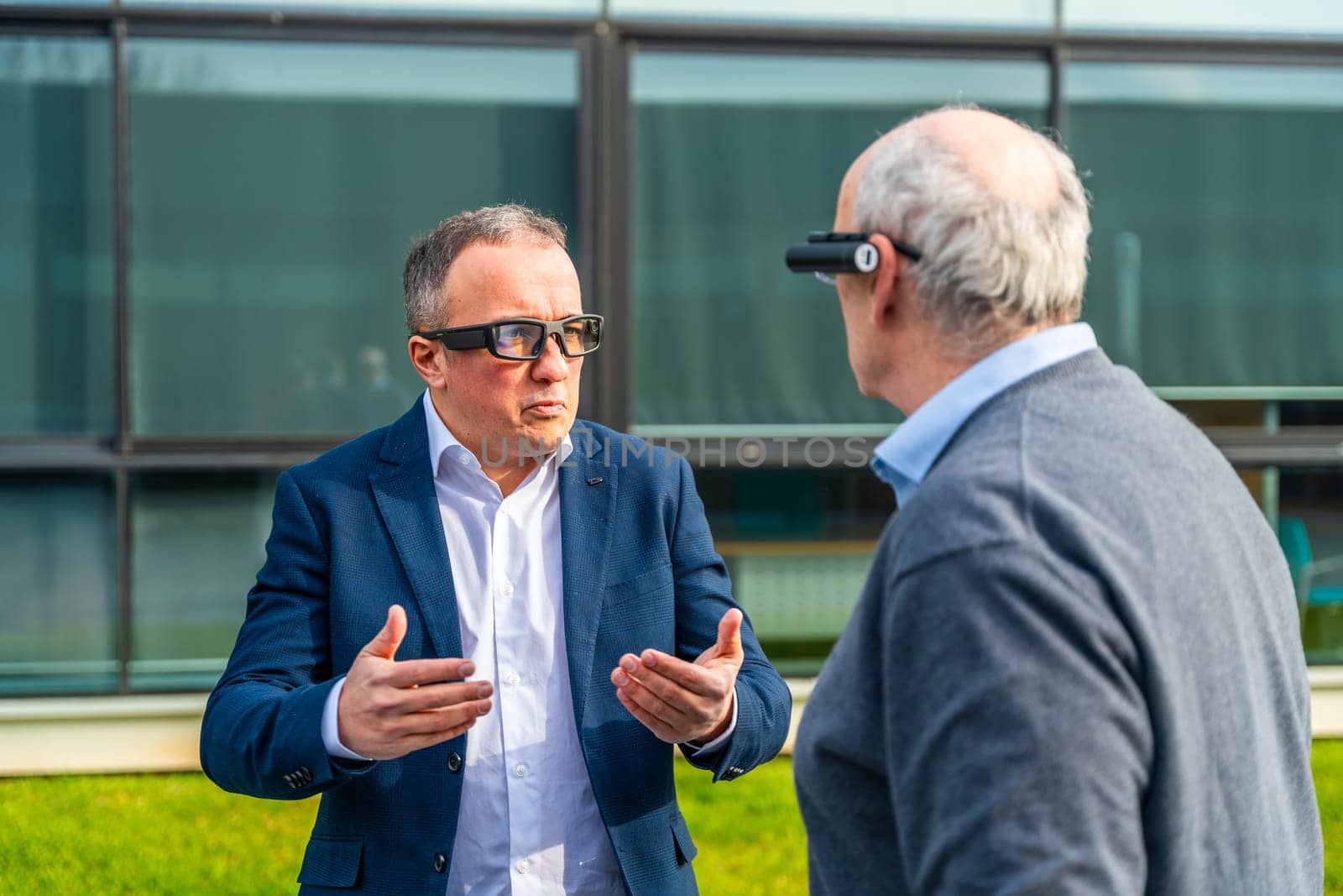 Aged businessmen coworkers using an augmented reality device while talking outdoors