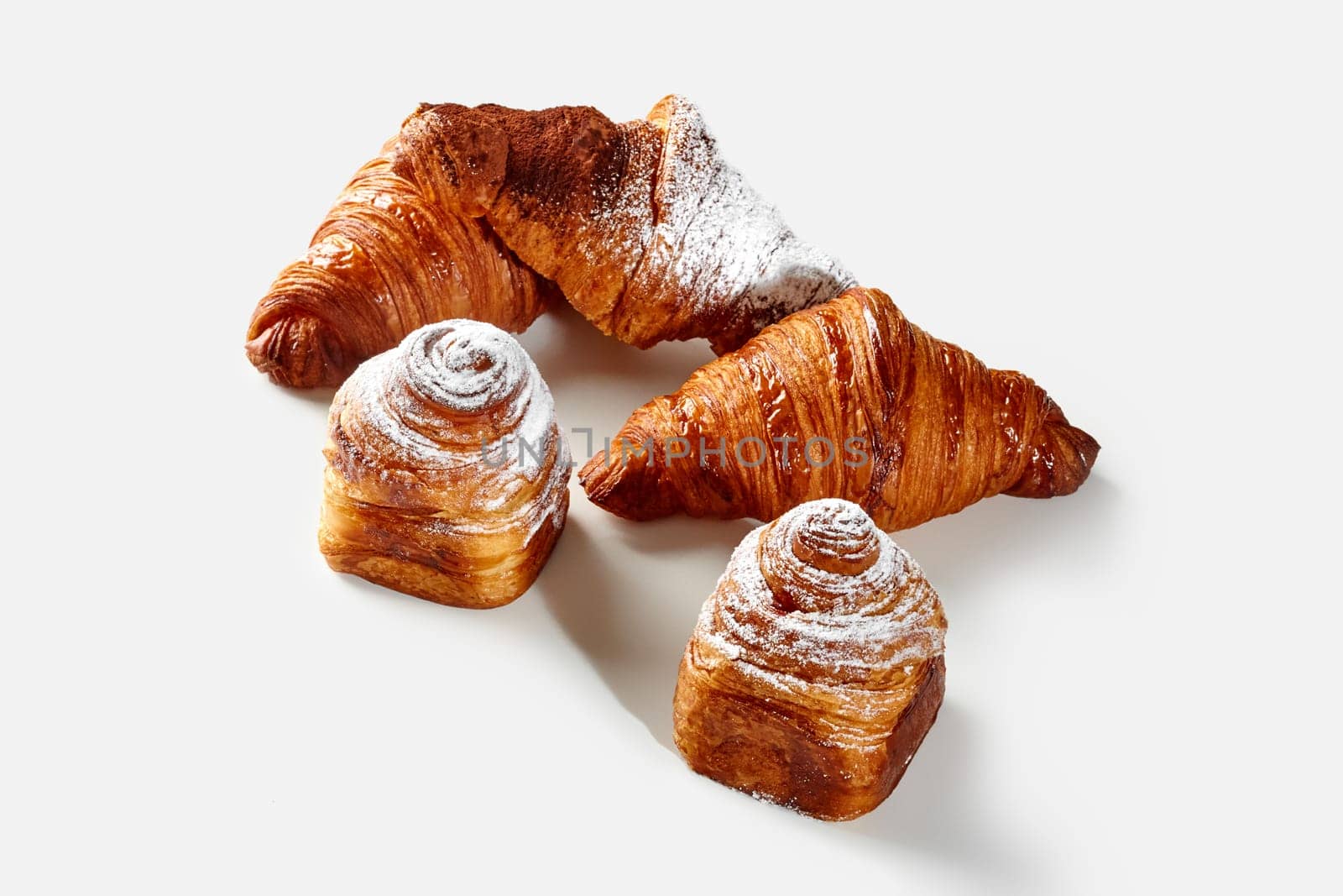 Delightful golden flaky classic croissants and cube shaped cruffins, dusted with powdered sugar and cocoa, arranged on white background. Sweet French style pastries