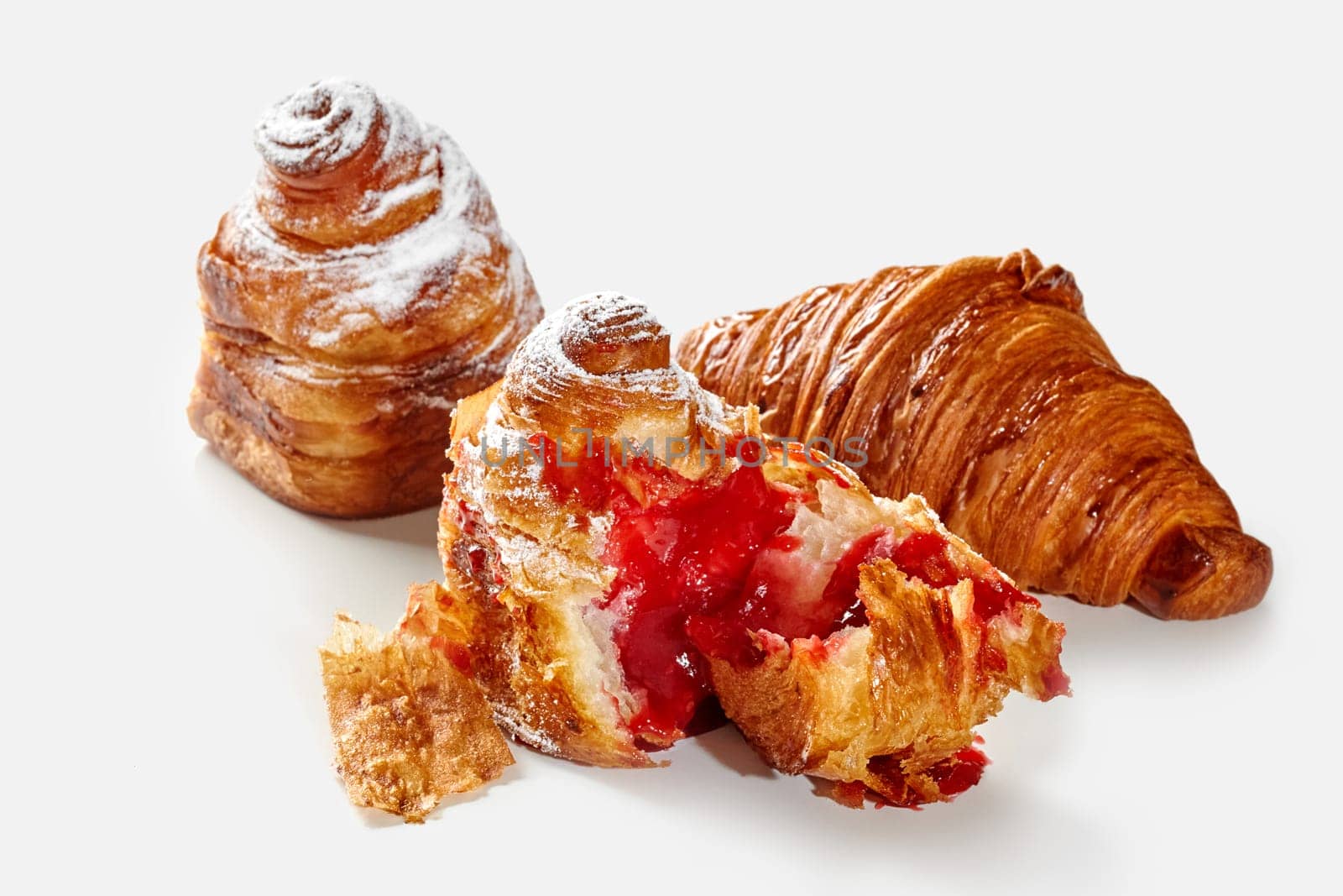 Delightful golden flaky croissant and cube shaped cruffins, dusted with powdered sugar with sweet berry jam filling on white background. Sweet French style pastries