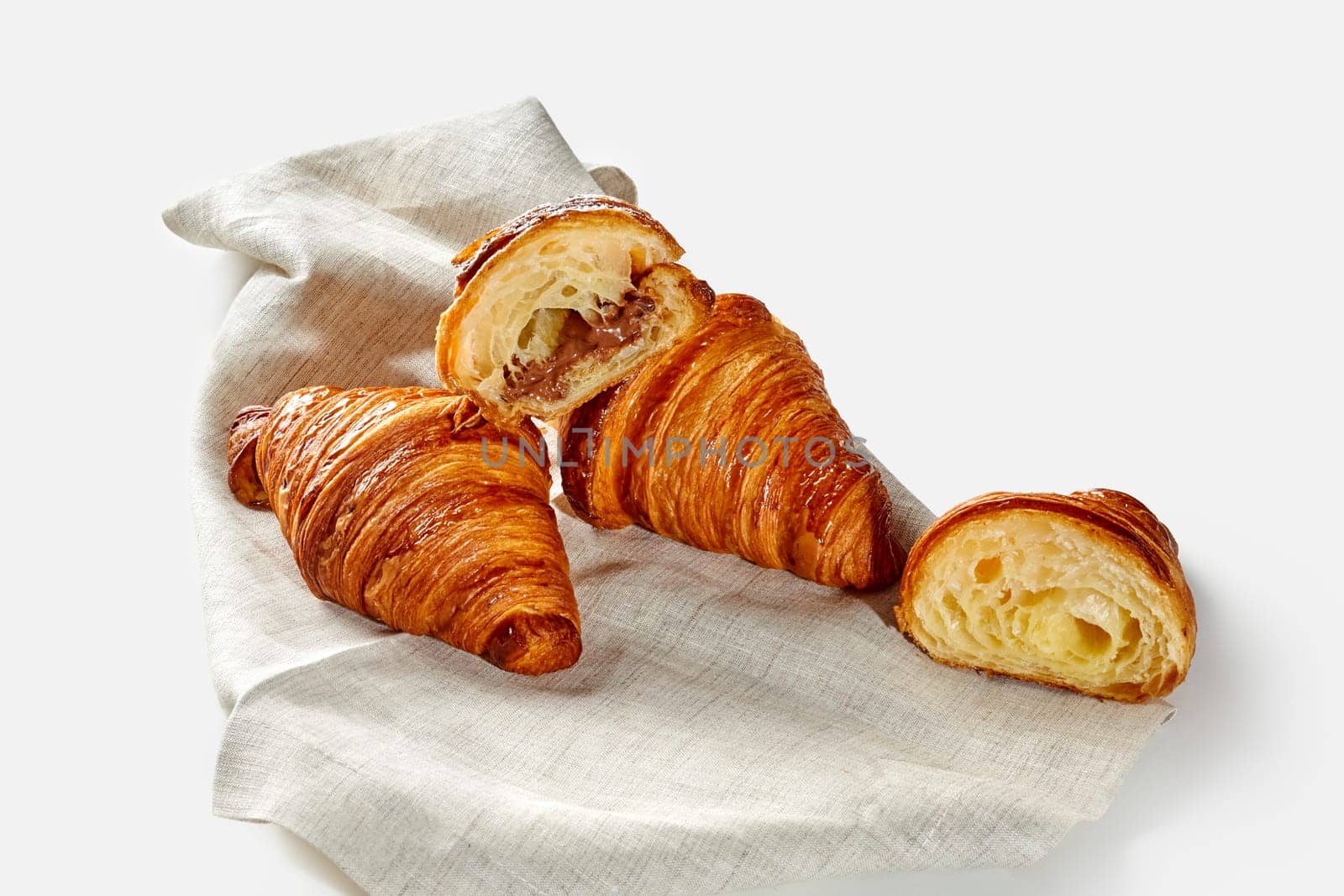 Flaky and delicately sweet croissants with nut and chocolate filling arranged on linen cloth, isolate on white background. Modern confectionery in classic French tradition