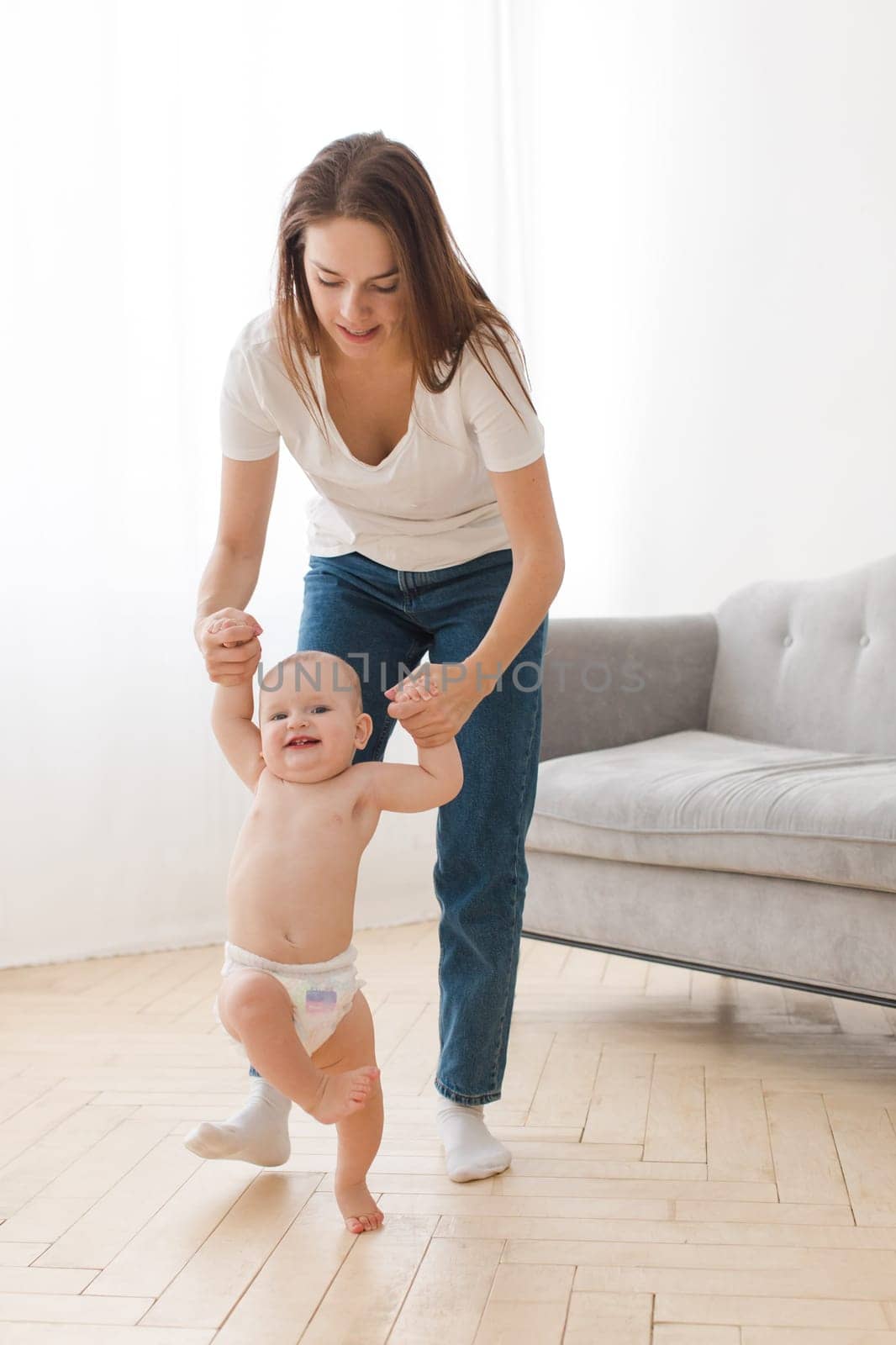 Adult woman taking care and teaching adorable toddler how to walk.