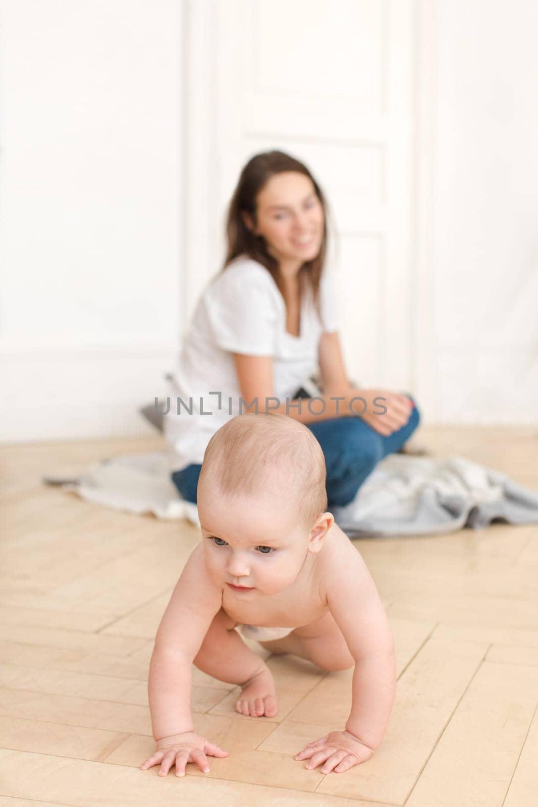 Happy mother watching little infant crawling on wooden floor at home looking concentrated.