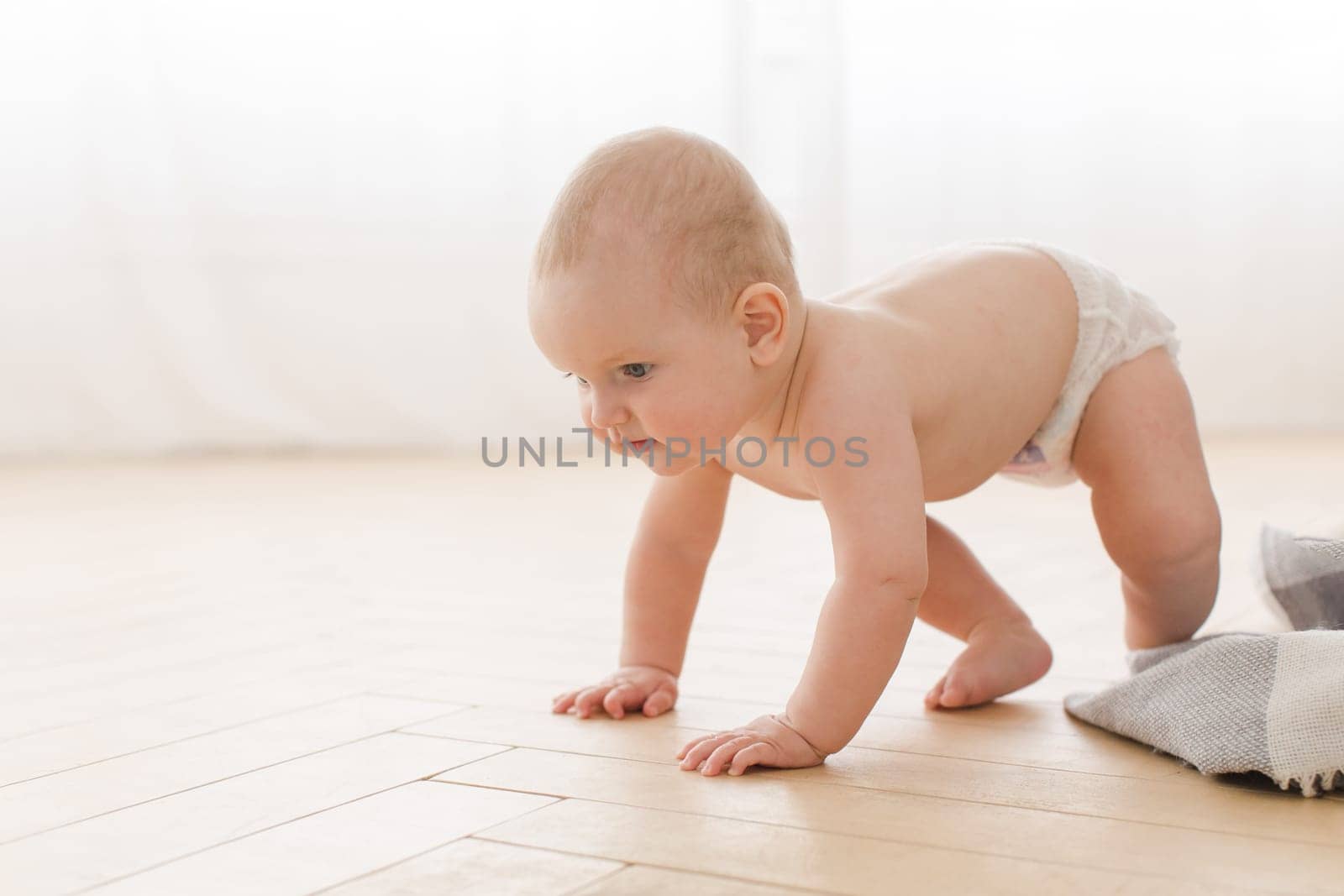 Small adorable infant standing on all fours on wooden floor at home.