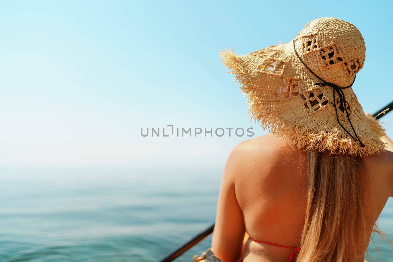 Woman in kayak back view. Happy woman with long hair in a swimsuit and hat floating in kayak on the sea. Summer holiday vacation. Summer holidays vacation at sea