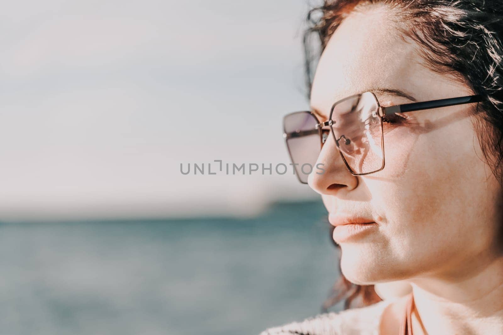 Portrait of a curly woman in glasses on the background of the sea. Vacation on the sea, walk, tourism