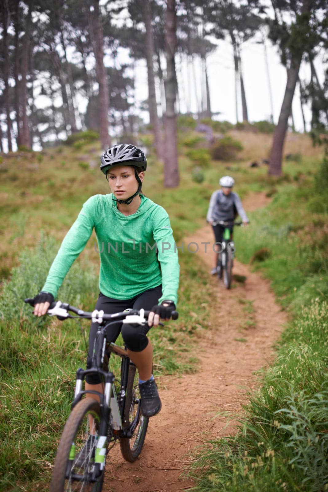 Woman, bike and cycling outdoor on trail for exercise, workout or adventure in forest with fitness. People, cyclists and bicycle with helmet in woods or off road for sport, hobby and travel in nature.