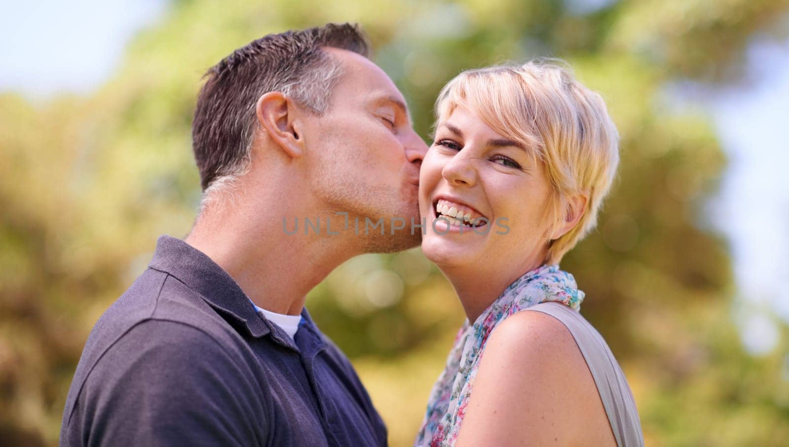 Portrait, couple and love with kiss in happiness on outdoor, affection and romance with date. Park, relationship and together with smile for bonding, care and trust with commitment for support by YuriArcurs