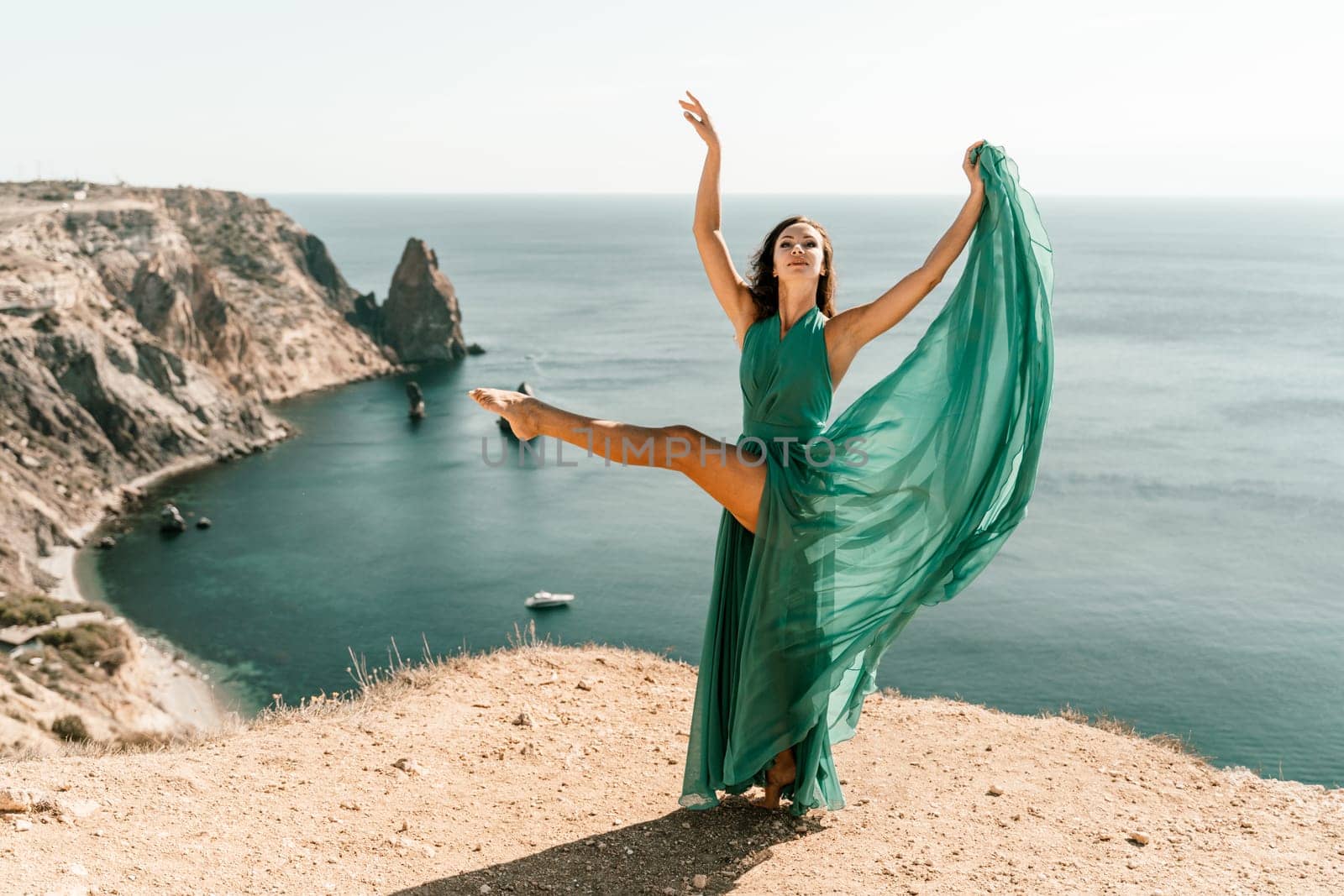 Woman green dress sea. Female dancer posing on a rocky outcrop high above the sea. Girl on the nature on blue sky background. Fashion photo