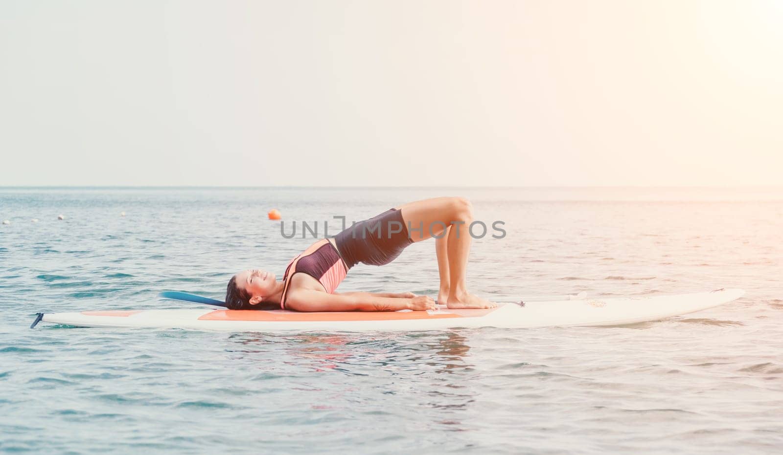 Woman sup yoga. Happy young sporty woman practising yoga pilates on paddle sup surfboard. Female stretching doing workout on sea water. Modern individual female outdoor summer sport activity. by panophotograph