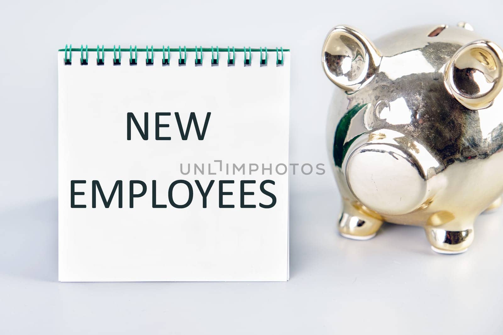 NEW EMPLOYEES Text written on a notebook on a gray background next to a piggy bank