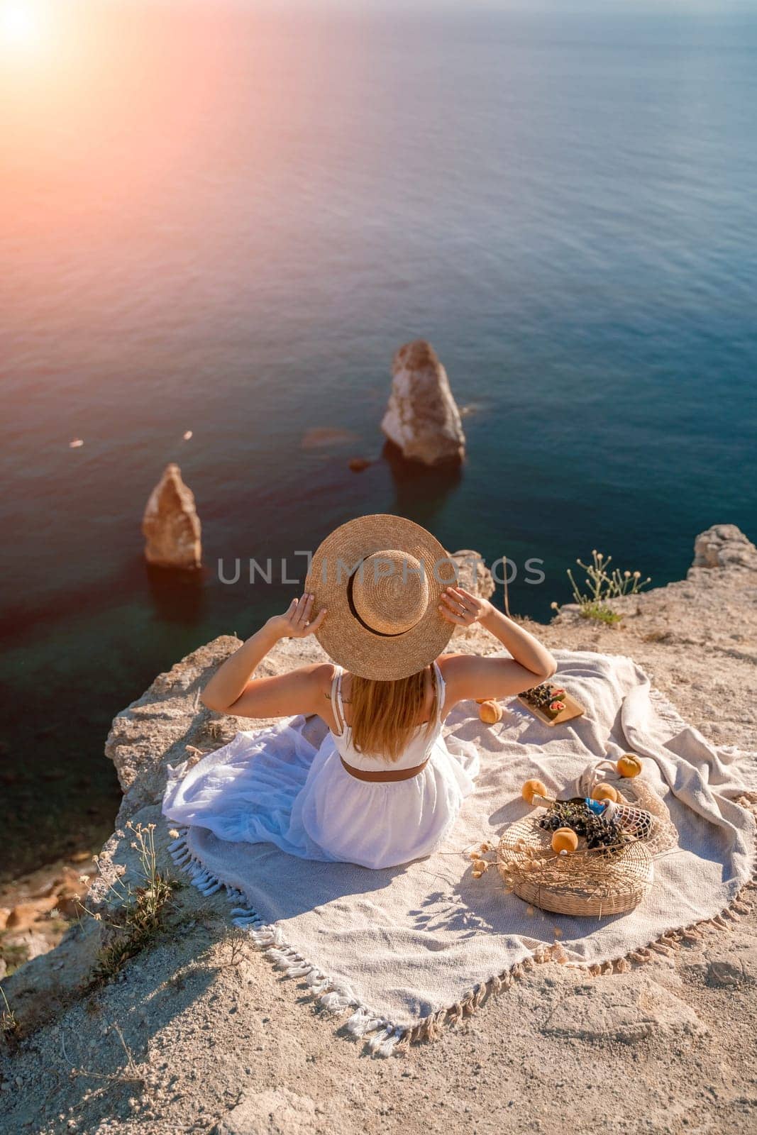 woman sea trevel. photo of a beautiful woman with long blond hair in a pink shirt and denim shorts and a hat having a picnic on a hill overlooking the sea.