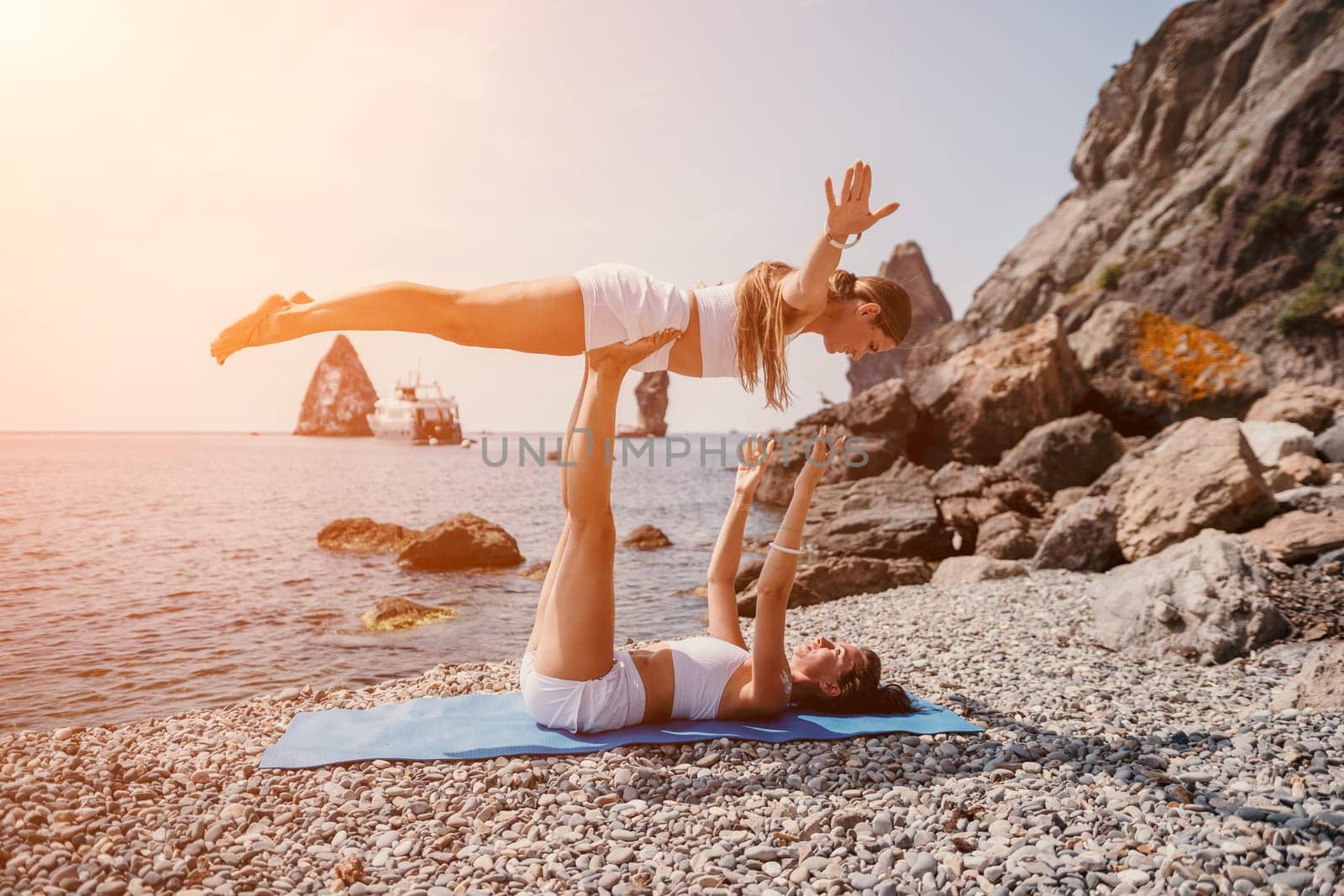 Woman sea yoga. Two happy women practicing yoga on the beach with ocean and rock mountains. Motivation and inspirational fit and exercising. Healthy lifestyle outdoors in nature, fitness concept. by panophotograph