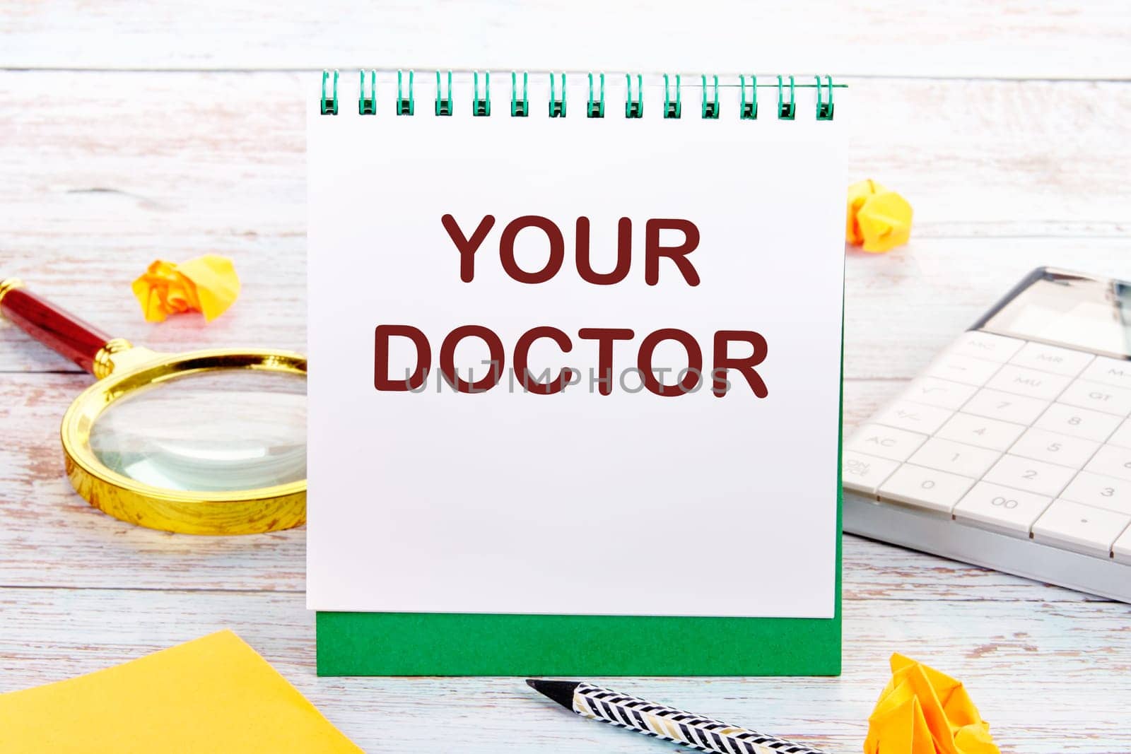 YOUR DOCTOR text on the white sheet of the notebook is next to a magnifying glass, calculator, pencil, stickers