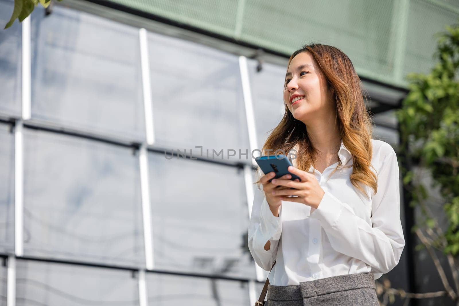 Happy young woman using smartphone outdoor on urban city street by Sorapop