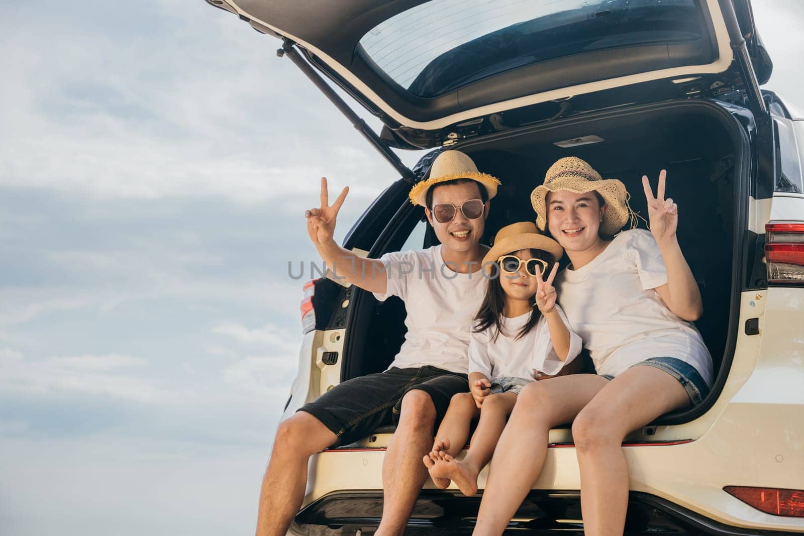 Family Day. Happy people having fun in summer vacation on beach, Family traveling in holiday at sea beach, Dad, mom and children daughter enjoying road trip sitting on back car showing V-sign signal