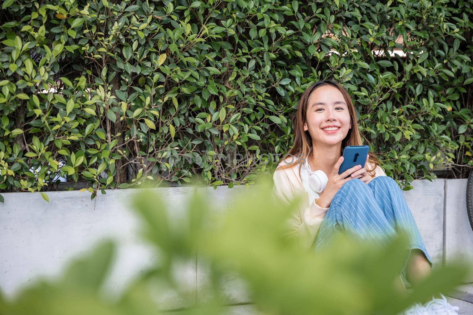 In the park a cheerful young woman with her bicycle enjoys a splendid spring day. She sits outdoors listening to music with earphones and happily types a joyful message on her mobile phone. by Sorapop