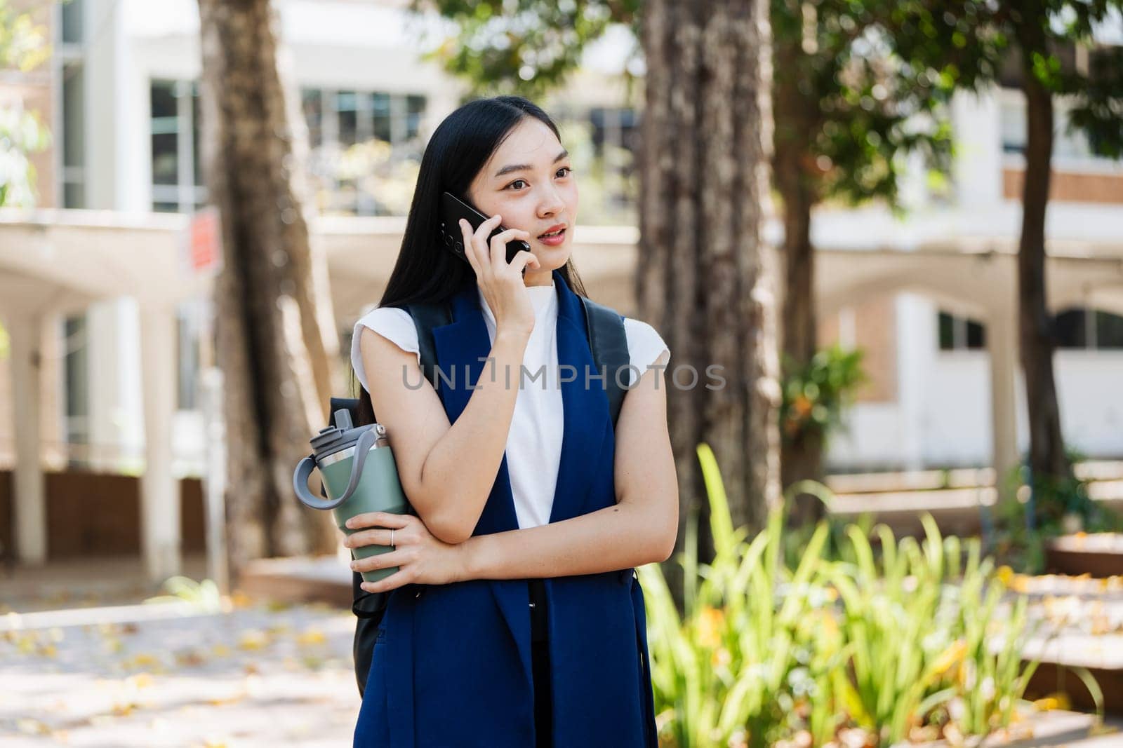 asian young businesswoman use smart phone with reusable eco-friendly ecological cup while commuting in city.