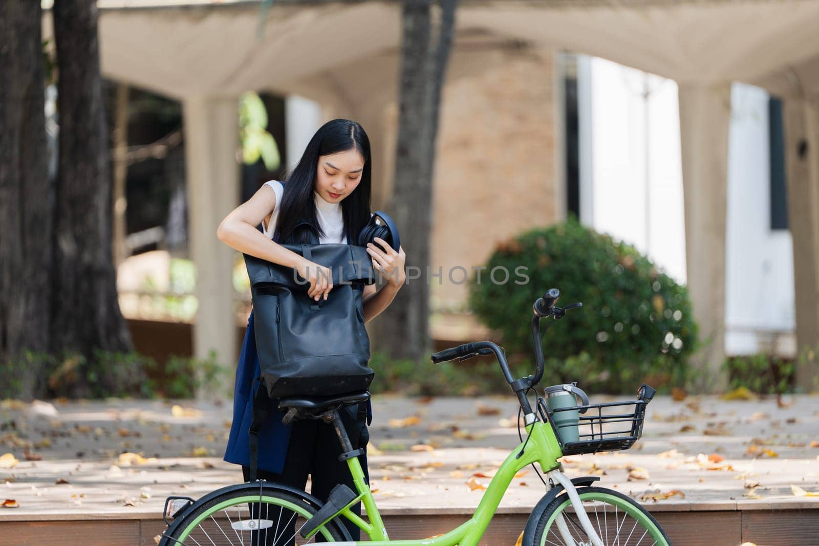 Asian young businesswoman bike to work for eco friendly green energy and listen music with headphone while commuting in city. Eco friendly by itchaznong