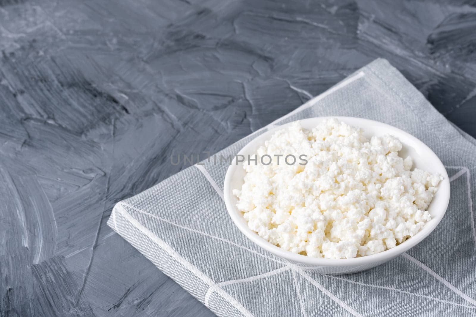 Cottage cheese in a white bowl on a grey background. Copy space.