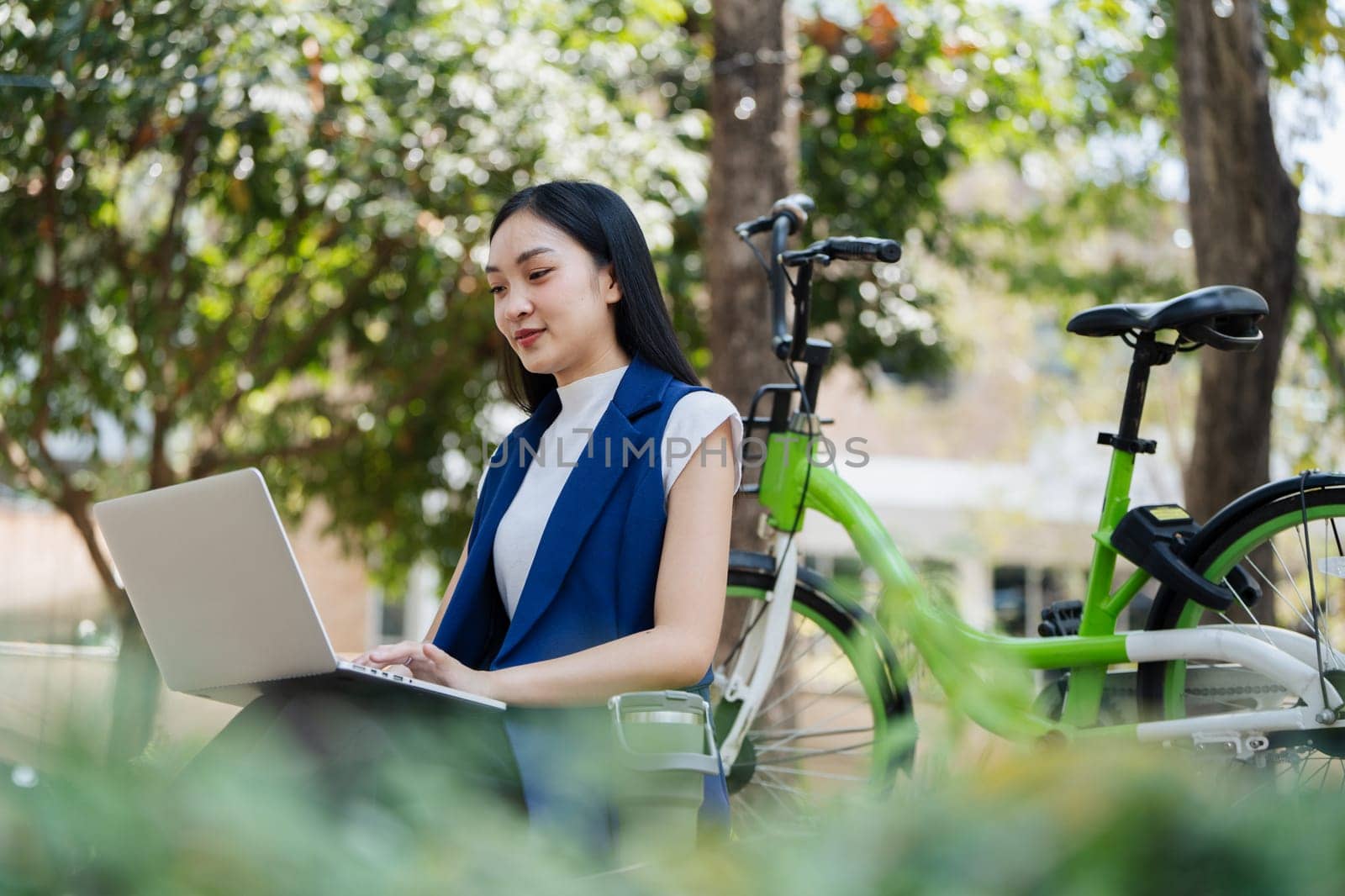 Young businesswoman sitting on stair in city park and using laptop for work hybrid. Bike to work eco friendly alternative vehicle green energy.