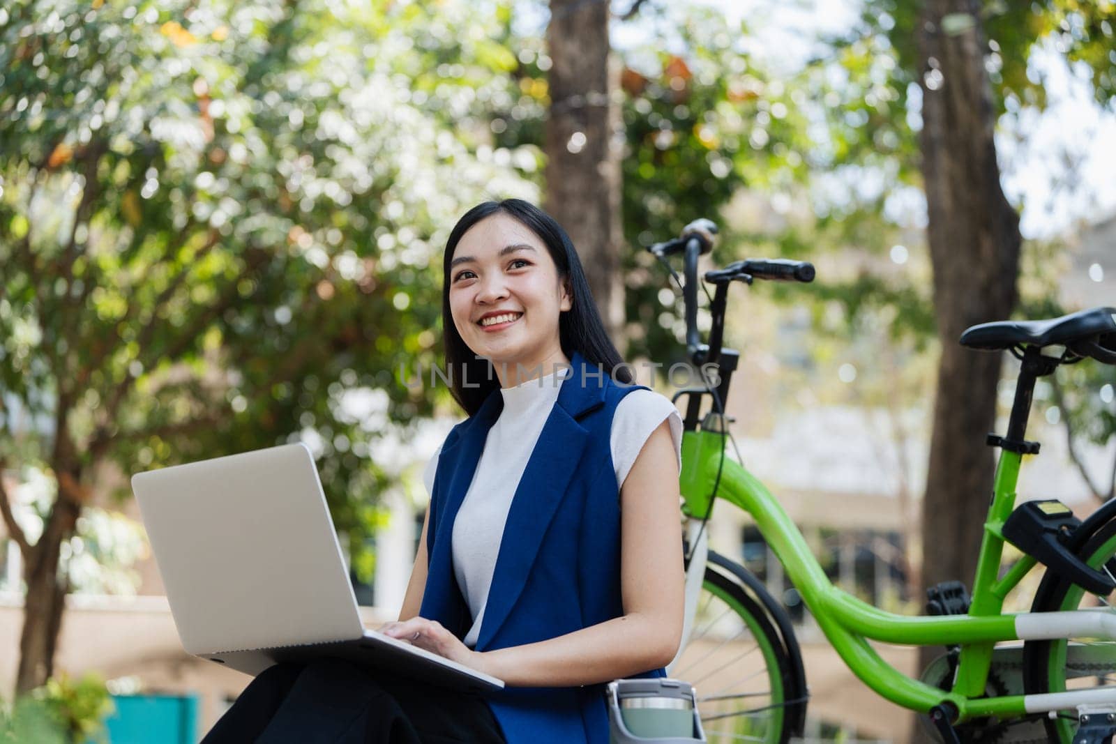 Young businesswoman sitting on stair in city park and using laptop for work hybrid. Bike to work eco friendly alternative vehicle green energy.