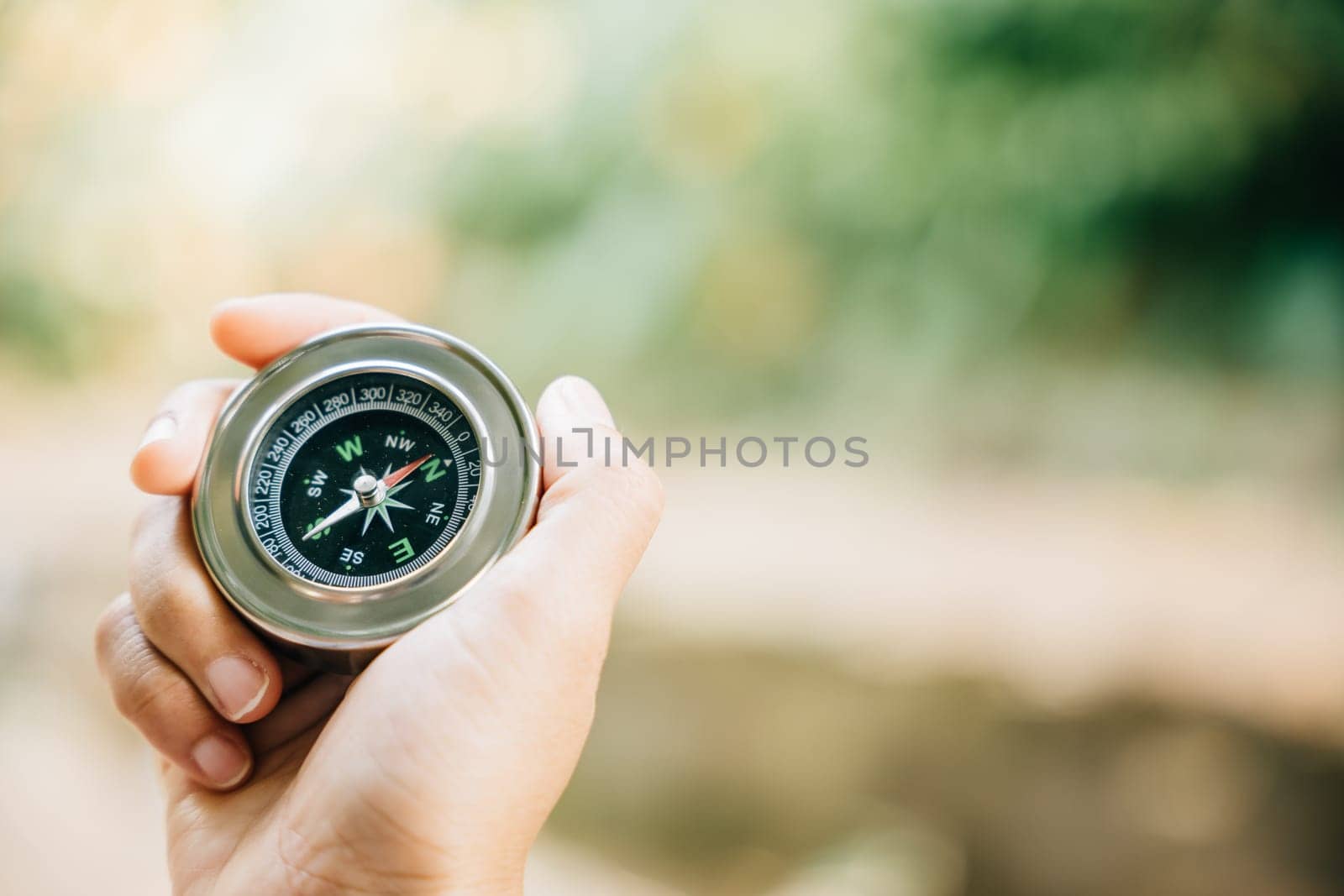 In the forest a hiker uses a compass to conquer confusion and find direction. The compass in the traveler hand represents topography and discovery amidst nature beauty. by Sorapop