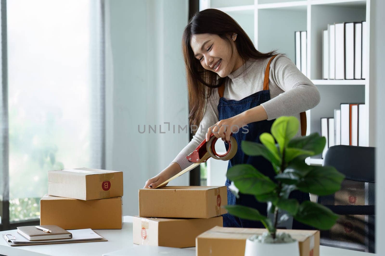 Young business entrepreneur sealing a box with tape. Preparing for shipping, Packing, online selling, e-commerce concept.