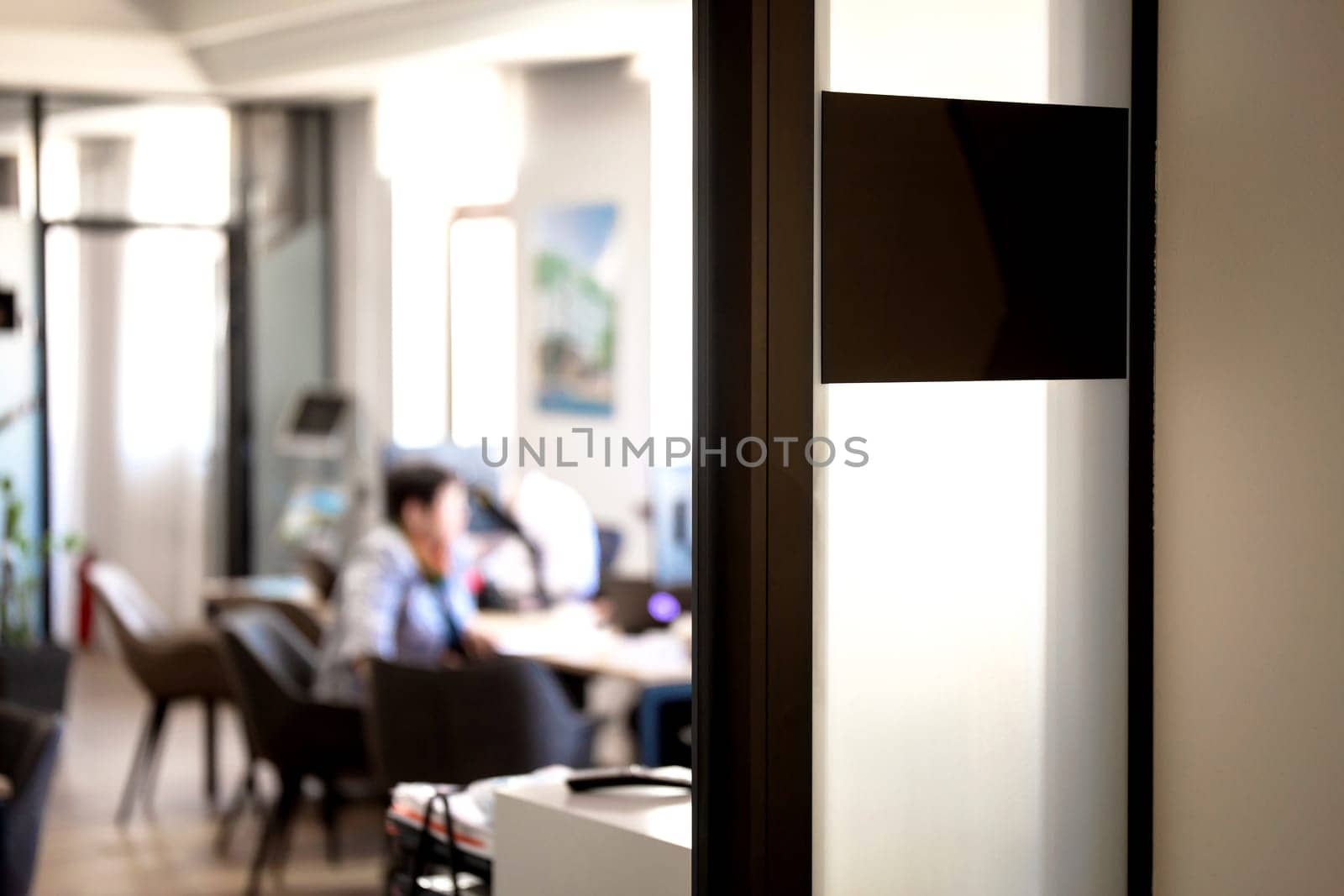A frosted glass panel on an office door provides a view of a busy office space with two people working at their desks.