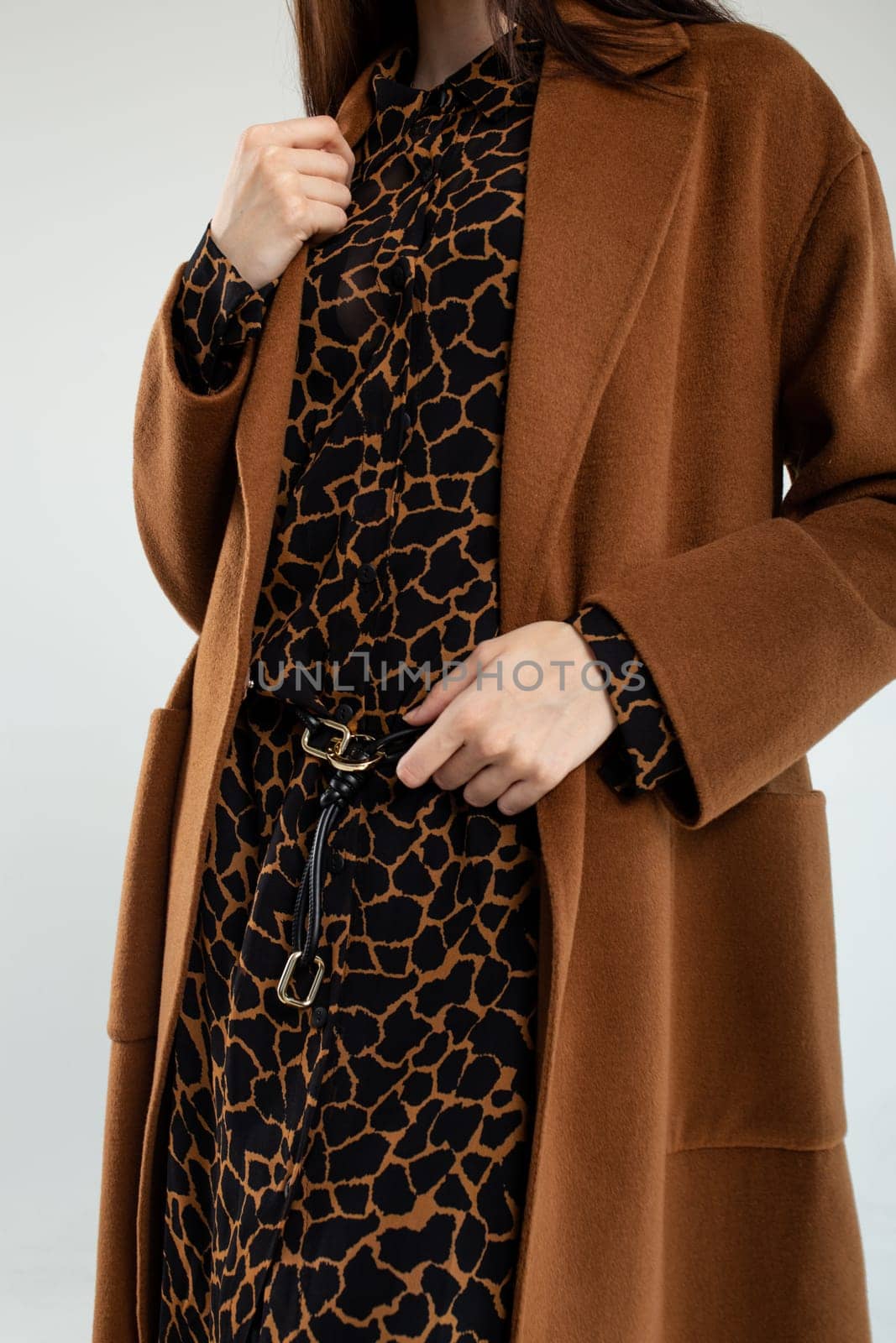 A stylish young woman is confidently posing in a trendy brown coat and fashionable animal print dress, showcasing elegance and modern style.