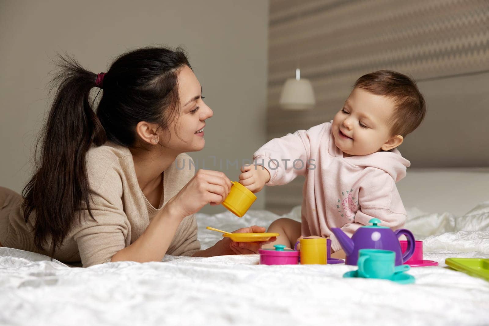 Attractive mother and cute little child daughter playing tea party in bedroom, family having fun