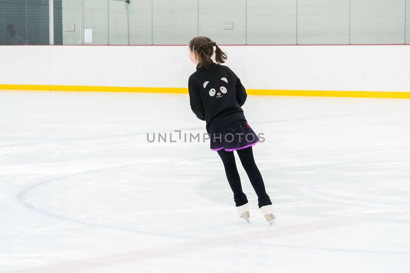 Young girl perfecting her figure skating routine while wearing her competition dress at an indoor ice rink.