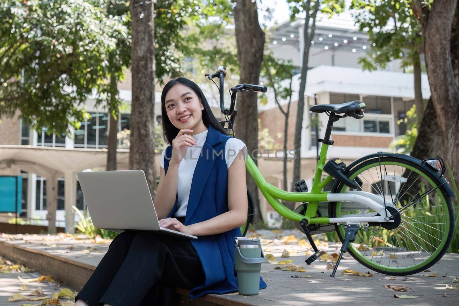 Asian business woman sitting and working in a nature park Travel by bicycle to save the environment.