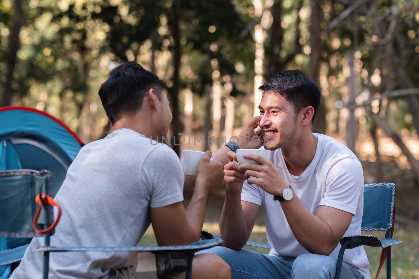 Asian LGBTQ couple drinking coffee in a romantic camping tent. LGBTQ couple drinking coffee in a camping tent, enjoying nature, forest, camping atmosphere, LGBTQ, gay, gay men..