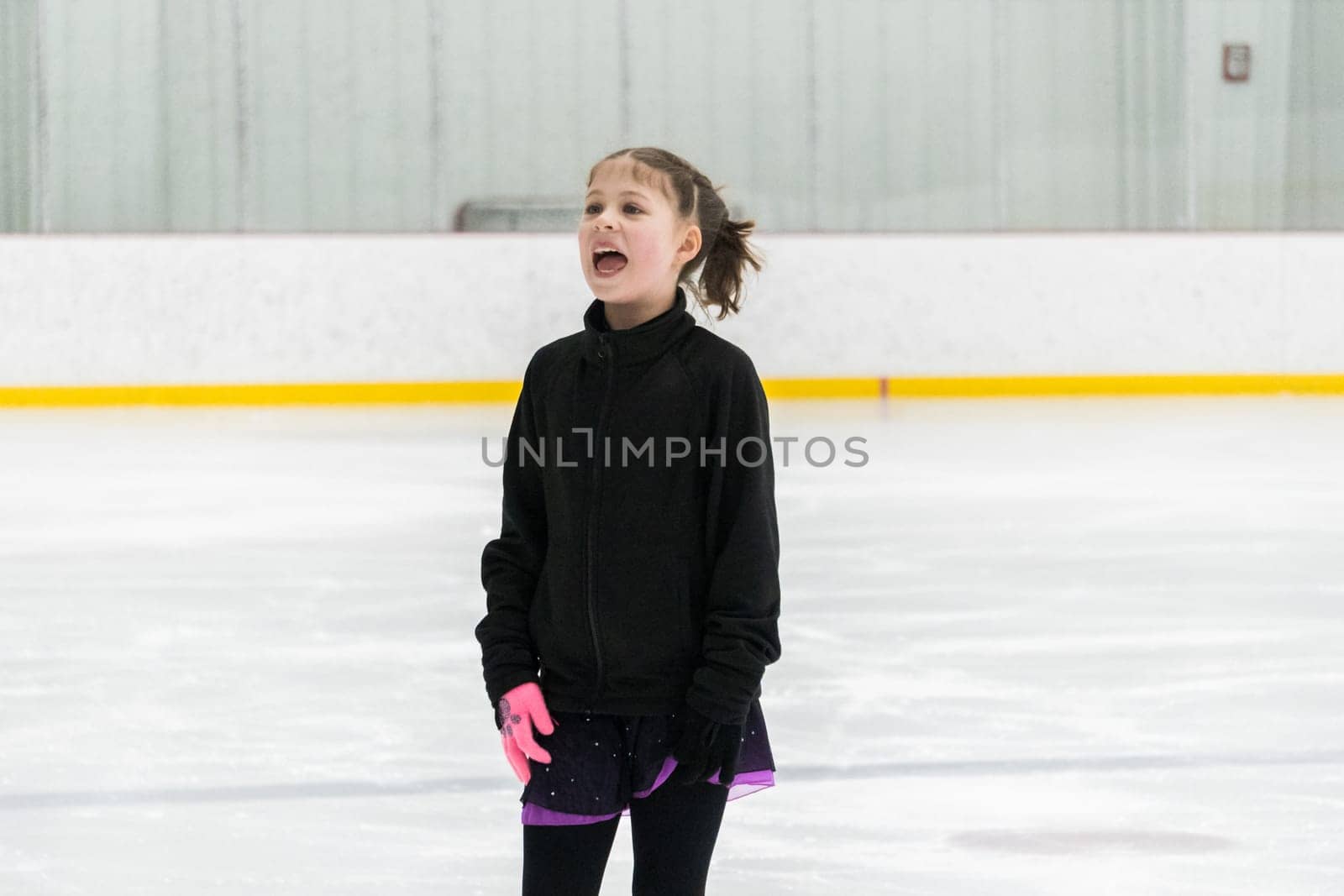 Young girl perfecting her figure skating routine while wearing her competition dress at an indoor ice rink.