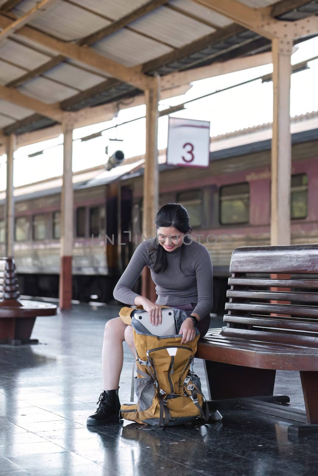 Young Asian tourist pack her things in her bag while waiting for her train at the train station. by wichayada