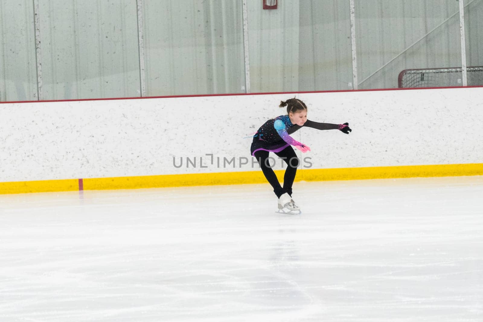 Young girl perfecting her figure skating routine while wearing her competition dress at an indoor ice rink.