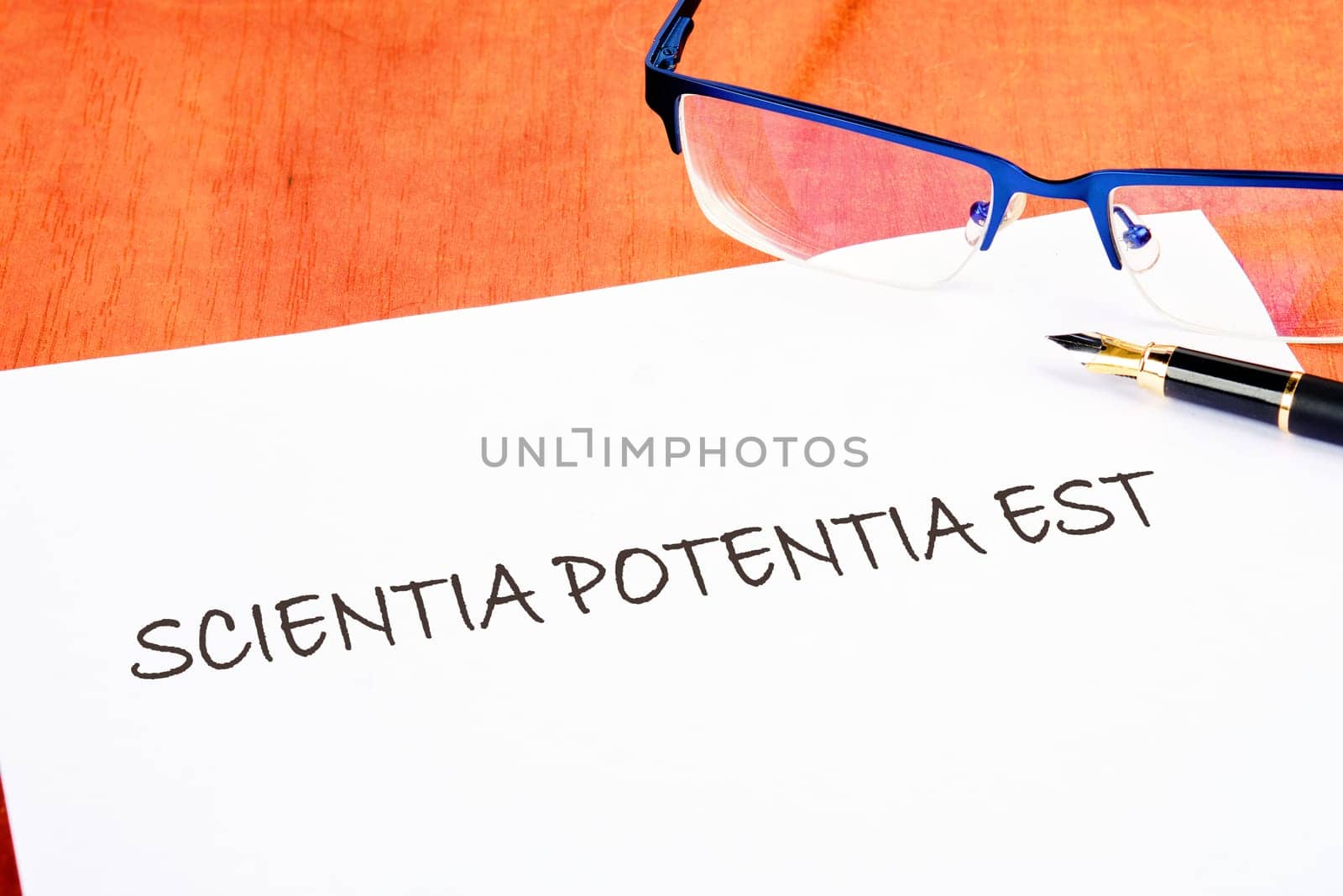 the phrase Scientia Potentia Est (Knowledge is power) written in Latin on a white piece of paper on the table next to the glasses