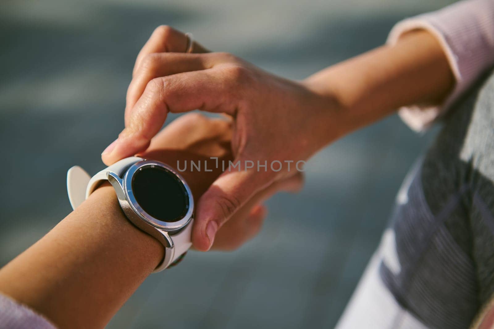 Close-up hands of female athlete checking application and heart rate on her smart watch during outdoor cardio workout. Selective focus on smart wristwatch of sportswoman with black blank mockup screen