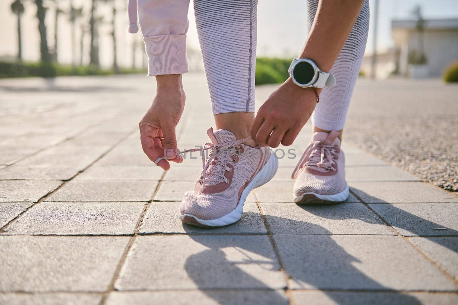 Cropped view of a fitness woman tying shoelaces before training, Getting ready for morning jog outdoor. People and sport by artgf