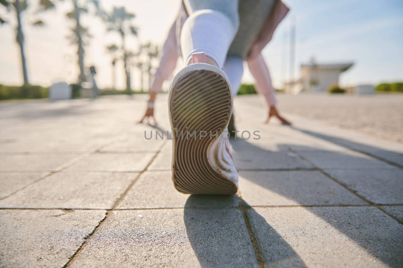 Cropped view of sportswoman feet in sports shoes, in start running position, getting ready for morning run on urban environment. Running. Jogging. Active healthy lifestyle. Fitness and dieting concept
