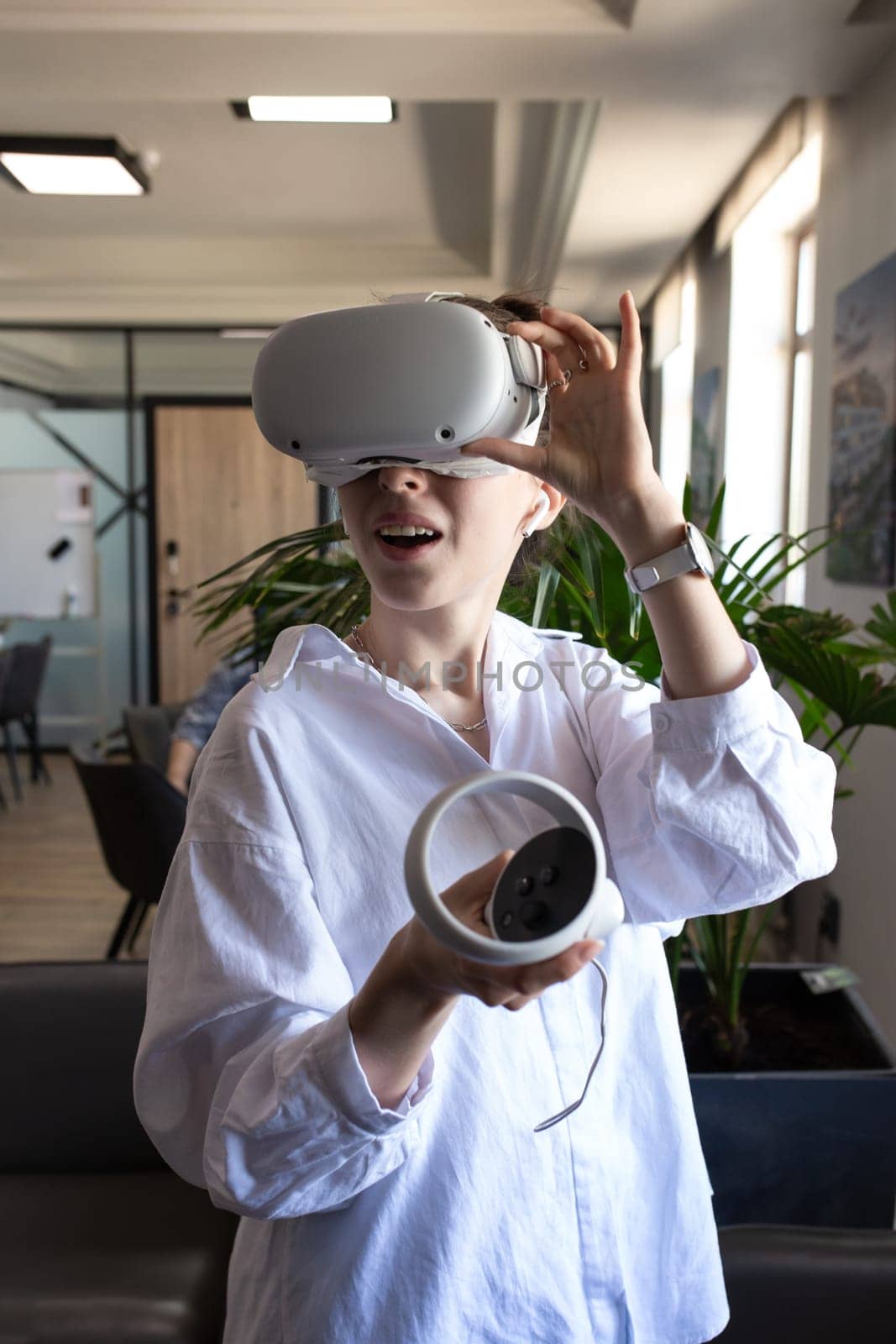 Young woman in professional attire testing new VR equipment in modern office, exploring virtual reality for business use.