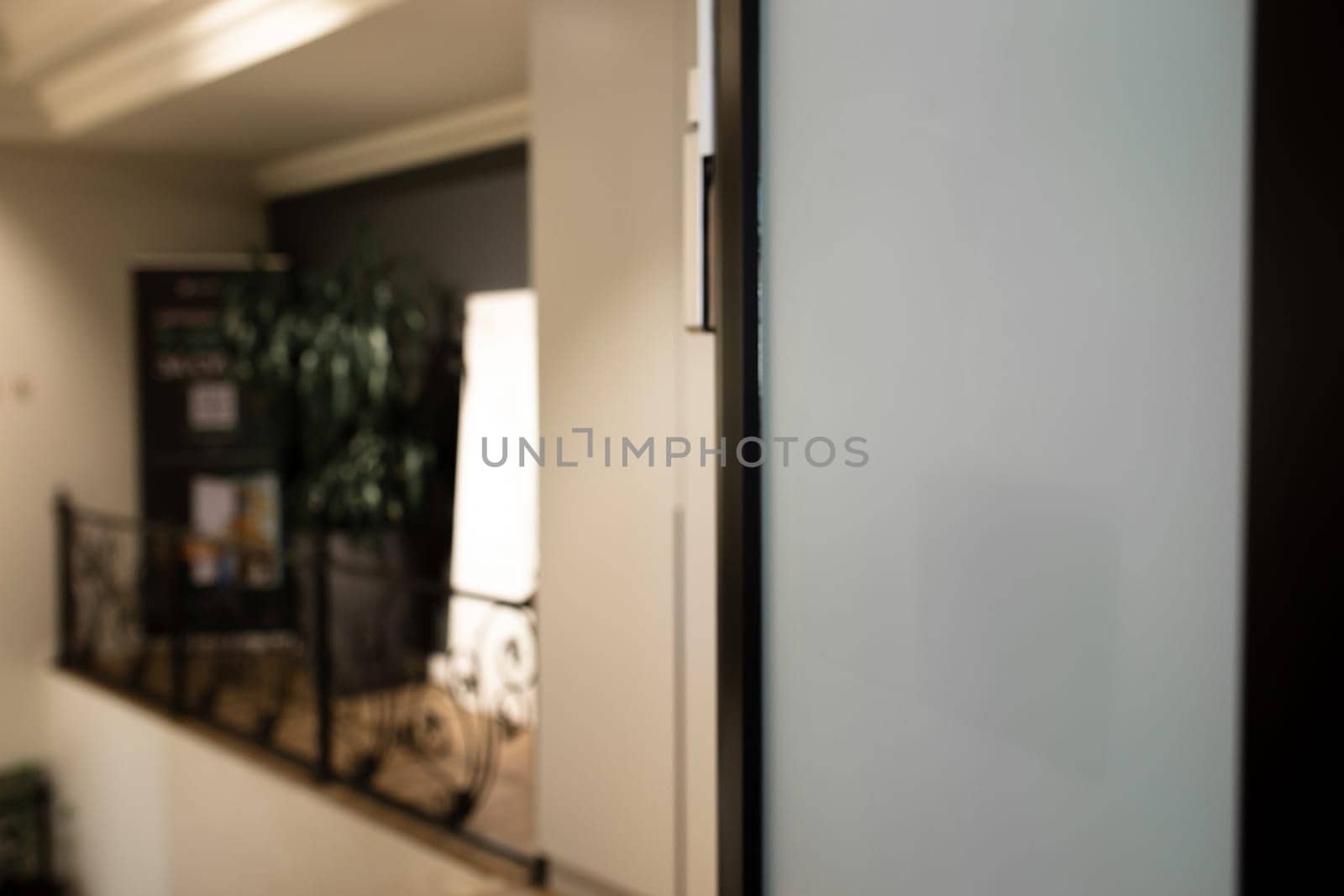 A frosted glass panel on an office door provides a view of a busy office space with two people working at their desks.