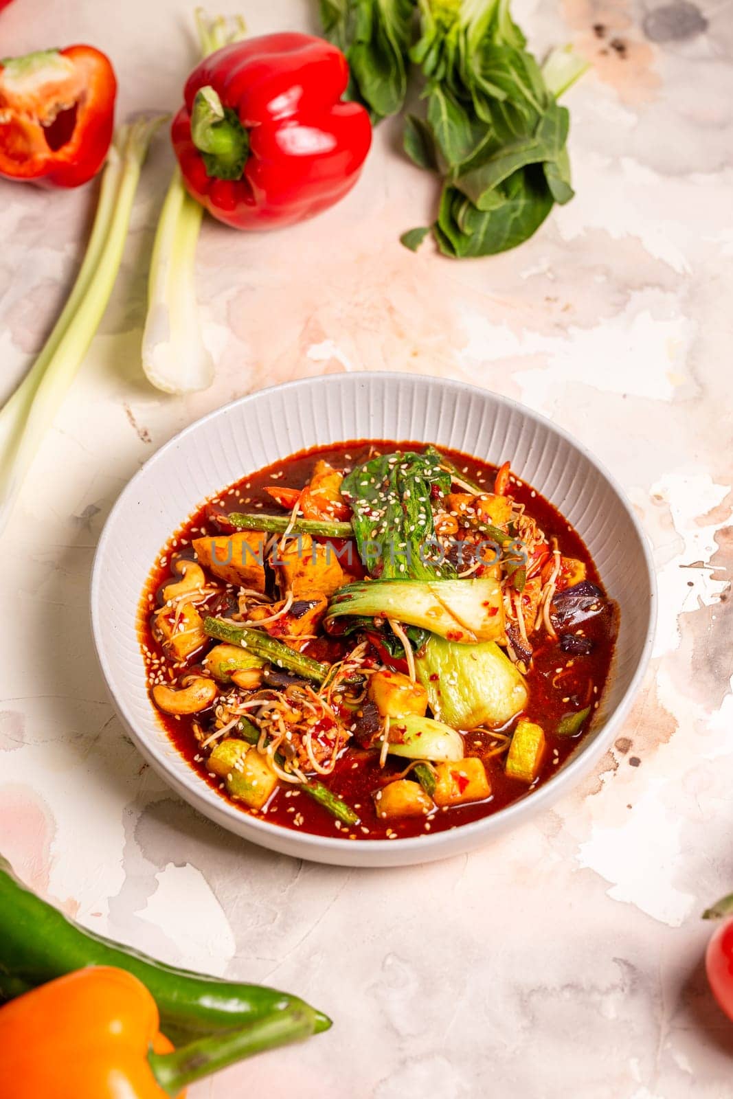 Red curry with veggies, tofu on a white background. Made with coconut milk, red curry paste, garnished with sesame seeds.