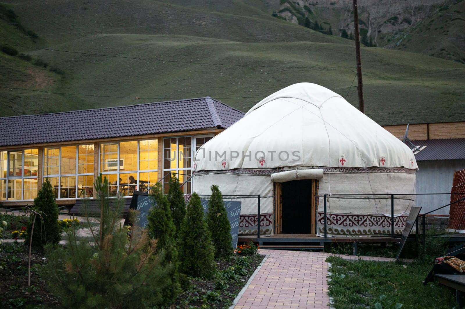 White yurt with red and brown traditional patterns on a green hill by Pukhovskiy