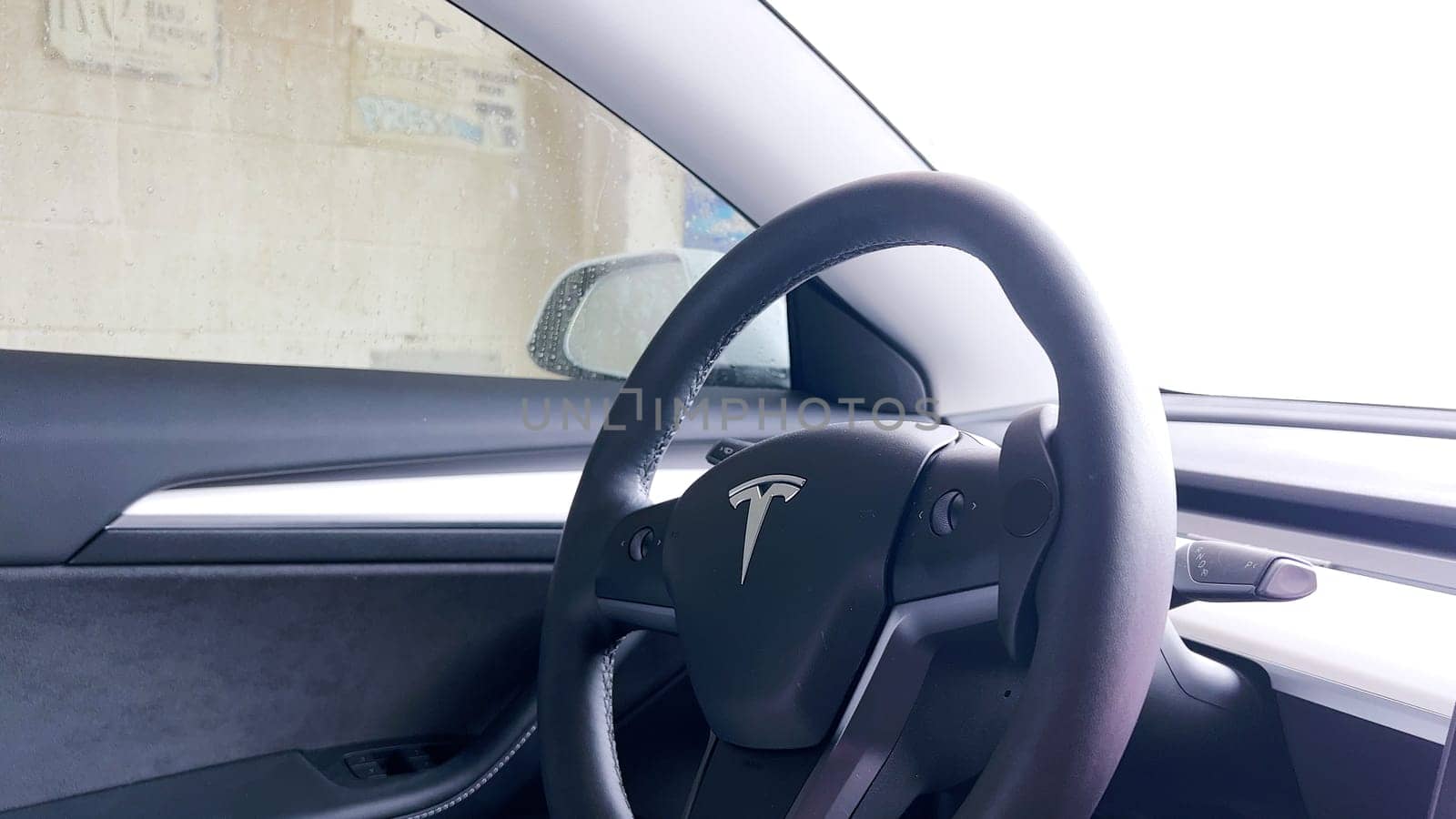 Denver, Colorado, USA-February 17, 2024-The interior of a Tesla Model 3 is shown from the driver’s perspective during a car wash, highlighting the vehicle’s modern design and dashboard display while water streams down the windshield.
