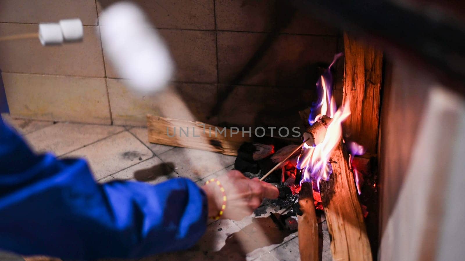 Marshmallows On Stick Roasting Over Campfire On Black Background. People take marshmallows around fireplace, enjoying their holiday. Hands of friends roasting marshmallows over fire in grill closeup. by Peruphotoart