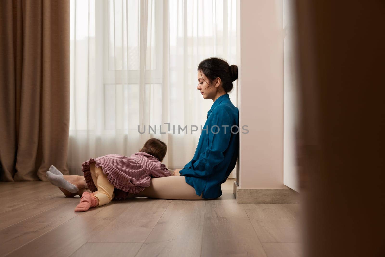 tired woman sitting on the floor with her little child girl at home